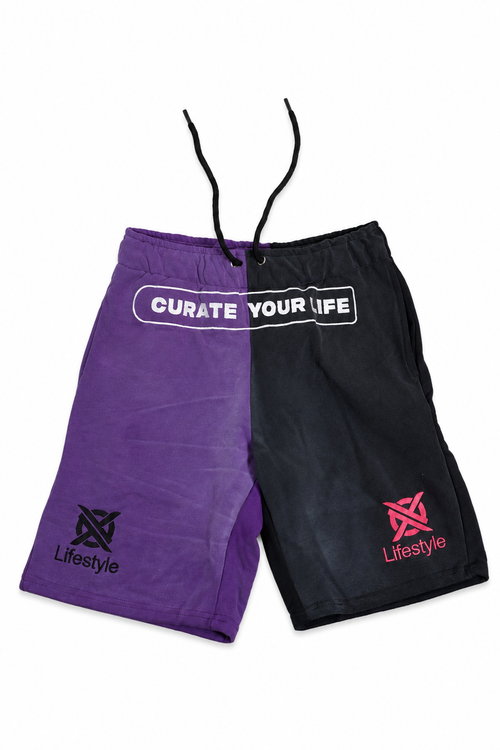A pair of split-color athletic shorts, one purple and one black, featuring a white graphic that reads 'CURATE YOUR LIFE' across the waistband and 'Lifestyle' branding with a stylized logo on the lower legs.